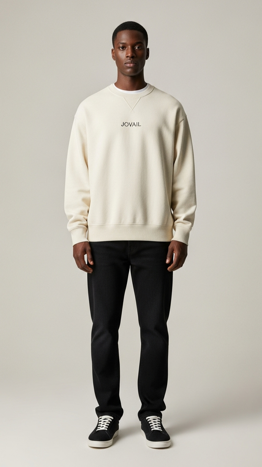 Man wearing a beige sweatshirt with text and black pants on a plain background