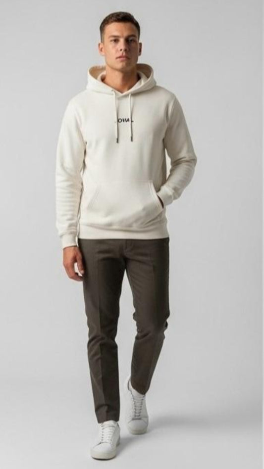 Man wearing a Cream hoodie with a brand logo, dark pants, and white sneakers on a light gray background