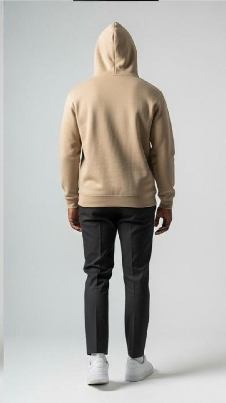 Person wearing a beige hoodie and dark pants on a plain background