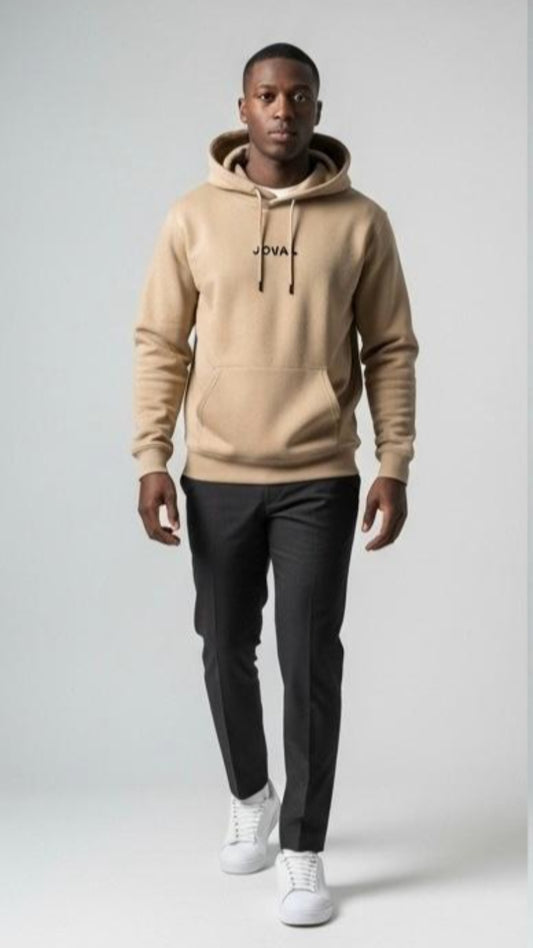 Man wearing a beige hoodie with a brand logo, black pants, and white sneakers on a light gray background